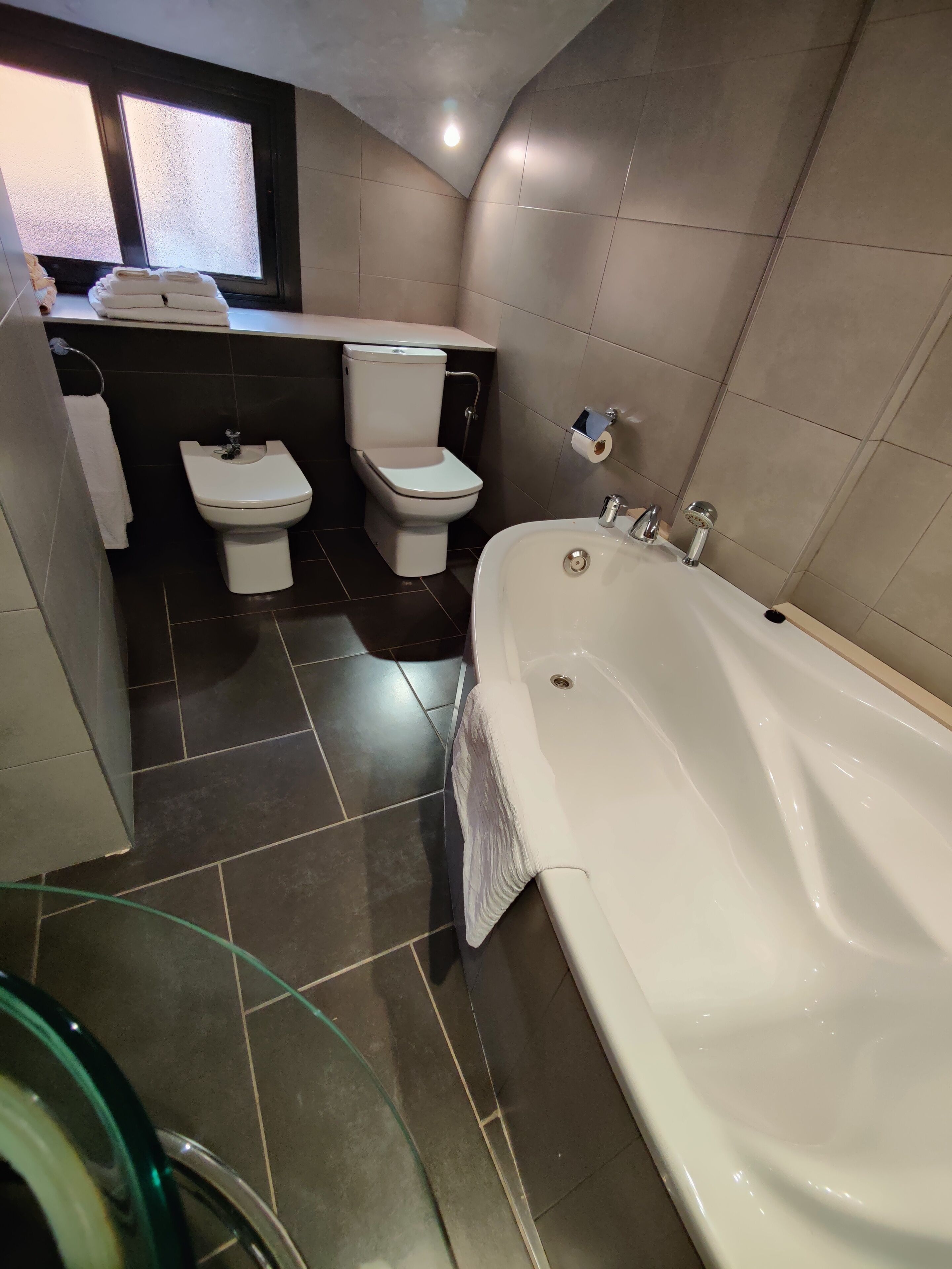 Un baño moderno con bañera, dos inodoros y una cabina de ducha de cristal.