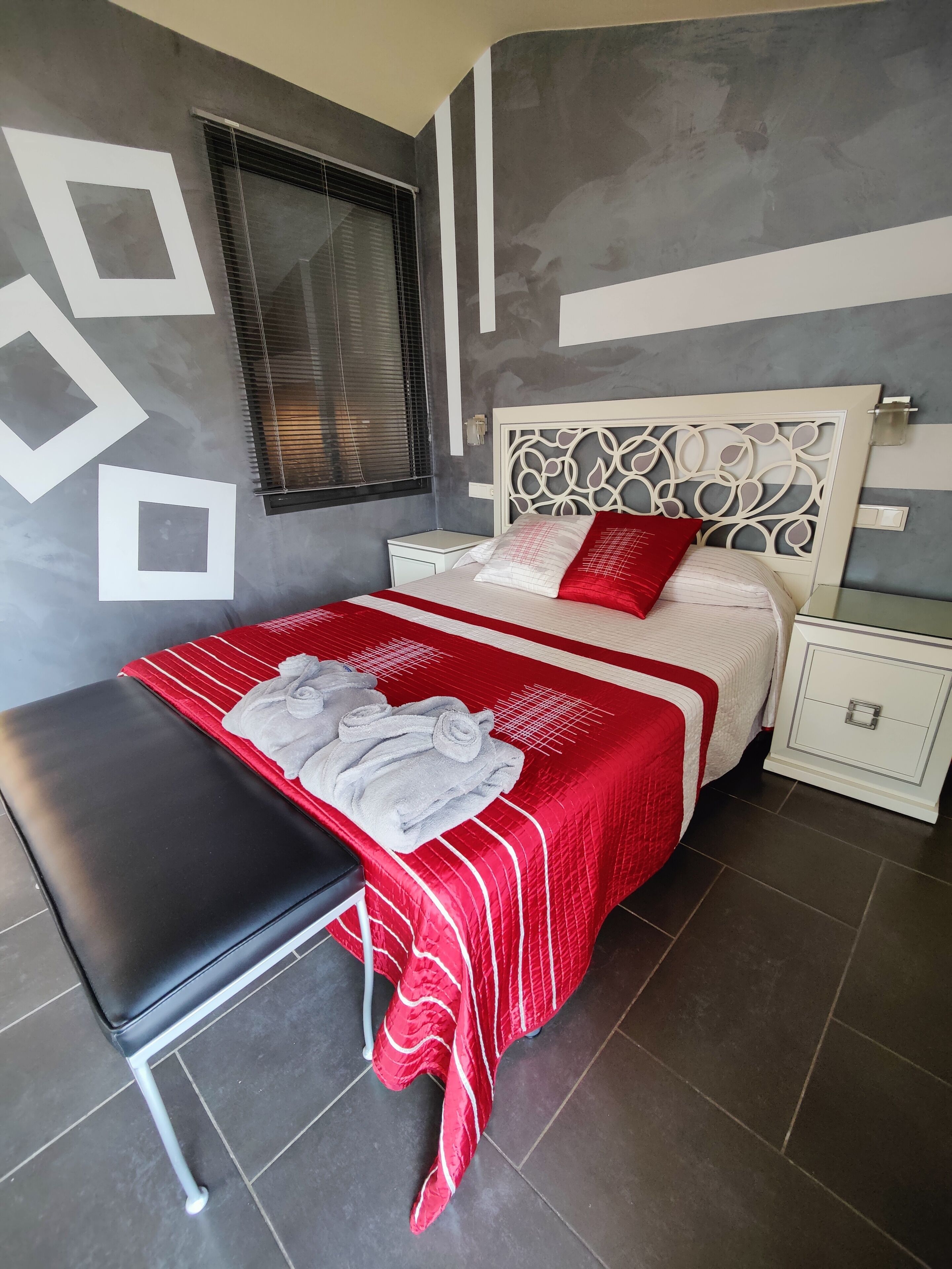 A neatly arranged bedroom with a bed, bedside tables, a bench, and a window with blinds.