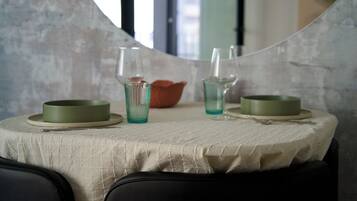 Una mesa de comedor con mantel blanco, dos platos verdes, dos vasos y un bol naranja pequeño.