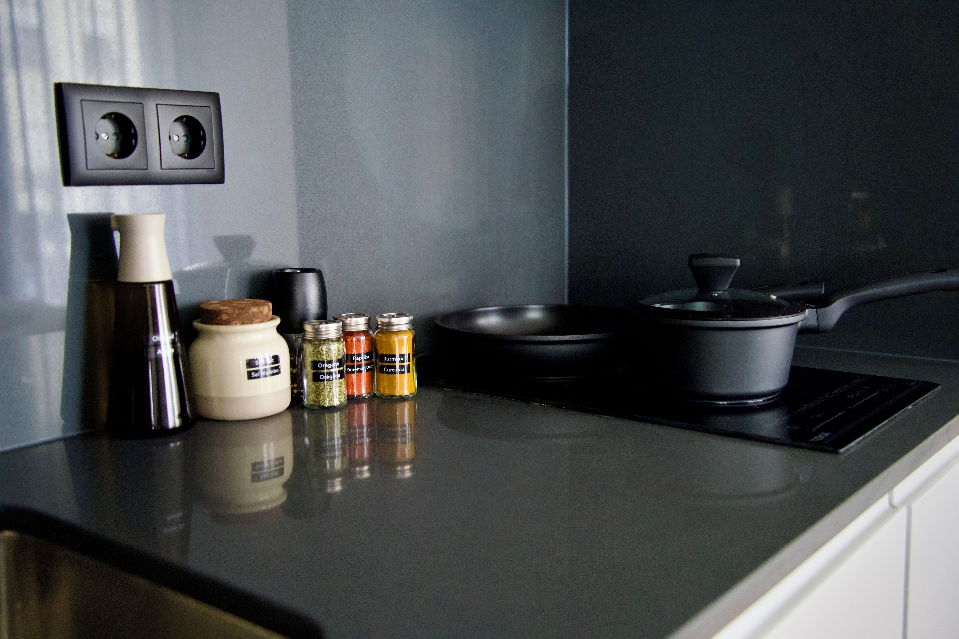 A kitchen counter with a black induction cooktop, a frying pan, a kettle, and several spice jars.
