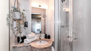 A modern bathroom with a marble sink, a glass shower enclosure, and a hanging plant. - Hotelfuchs (Saarbrücken)