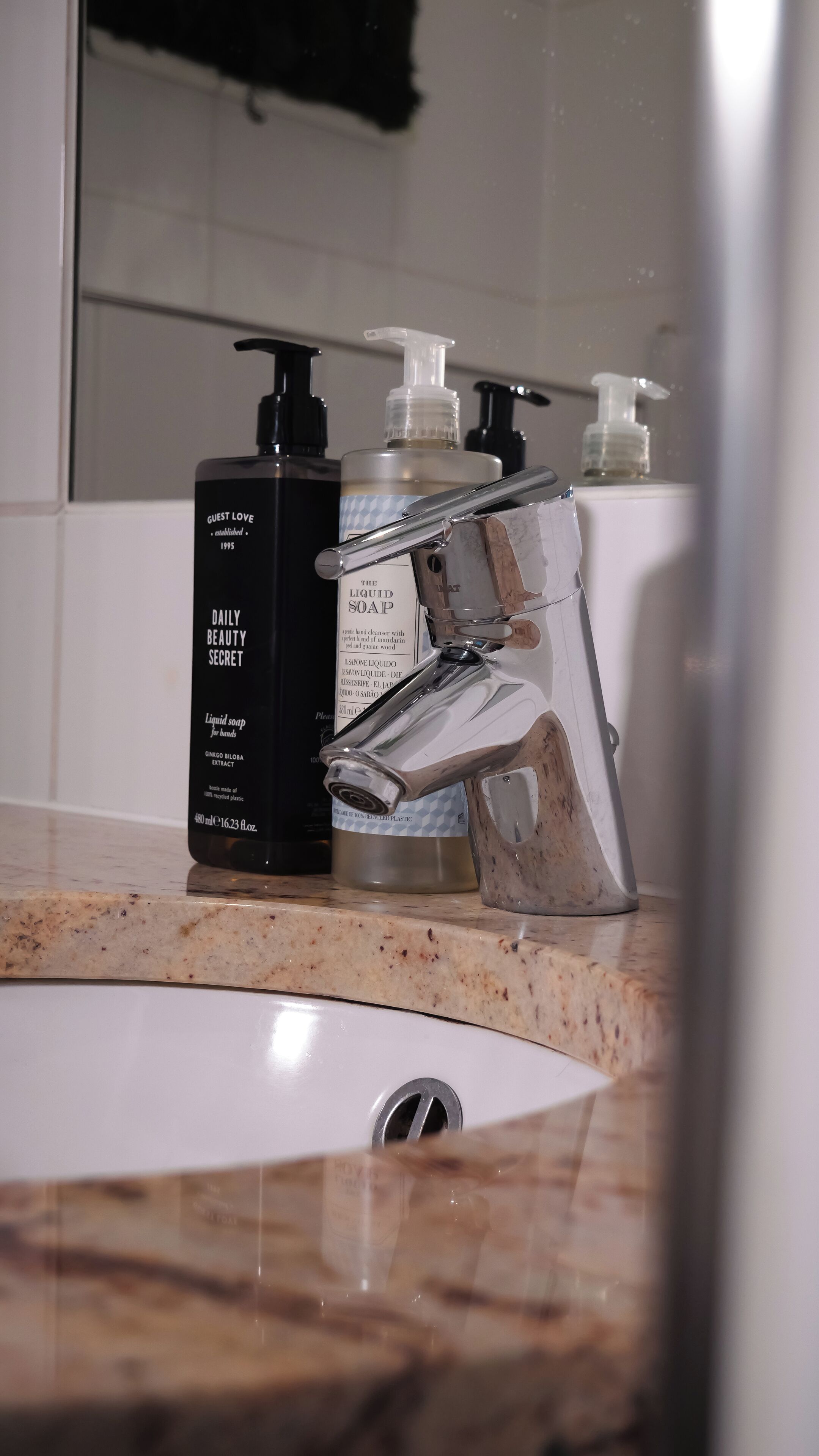 Un lavabo de salle de bain avec un robinet moderne, un flacon noir contenant du savon liquide et un flacon blanc contenant du savon liquide.