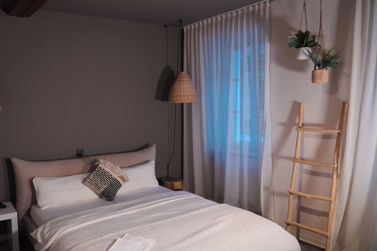 A bedroom with a bed, bedside tables, a hanging plant, and a wooden ladder.