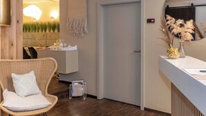 A modern interior with a wooden ceiling, a reception desk, a wicker chair, and a door with a towel hanging on it. - Hotelfuchs (Saarbrücken)