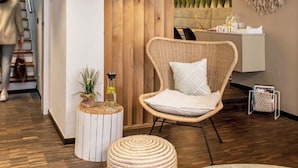 A modern living room with a wooden accent wall, a wicker chair, a round white side table, and a hanging pendant light. - Hotelfuchs (Saarbrücken)