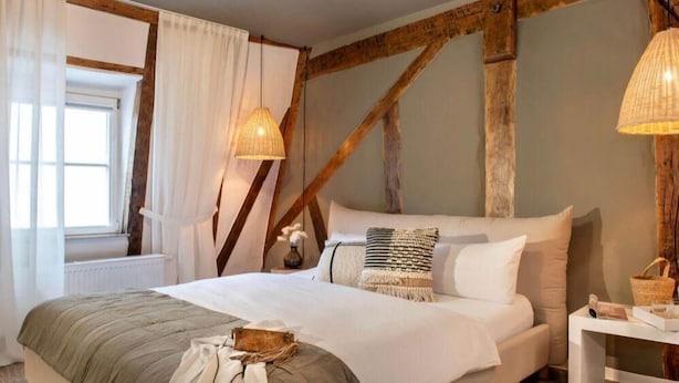 A bedroom with a large bed, wooden beams, a window with curtains, and a bedside lamp. - Hotelfuchs (Saarbrücken)
