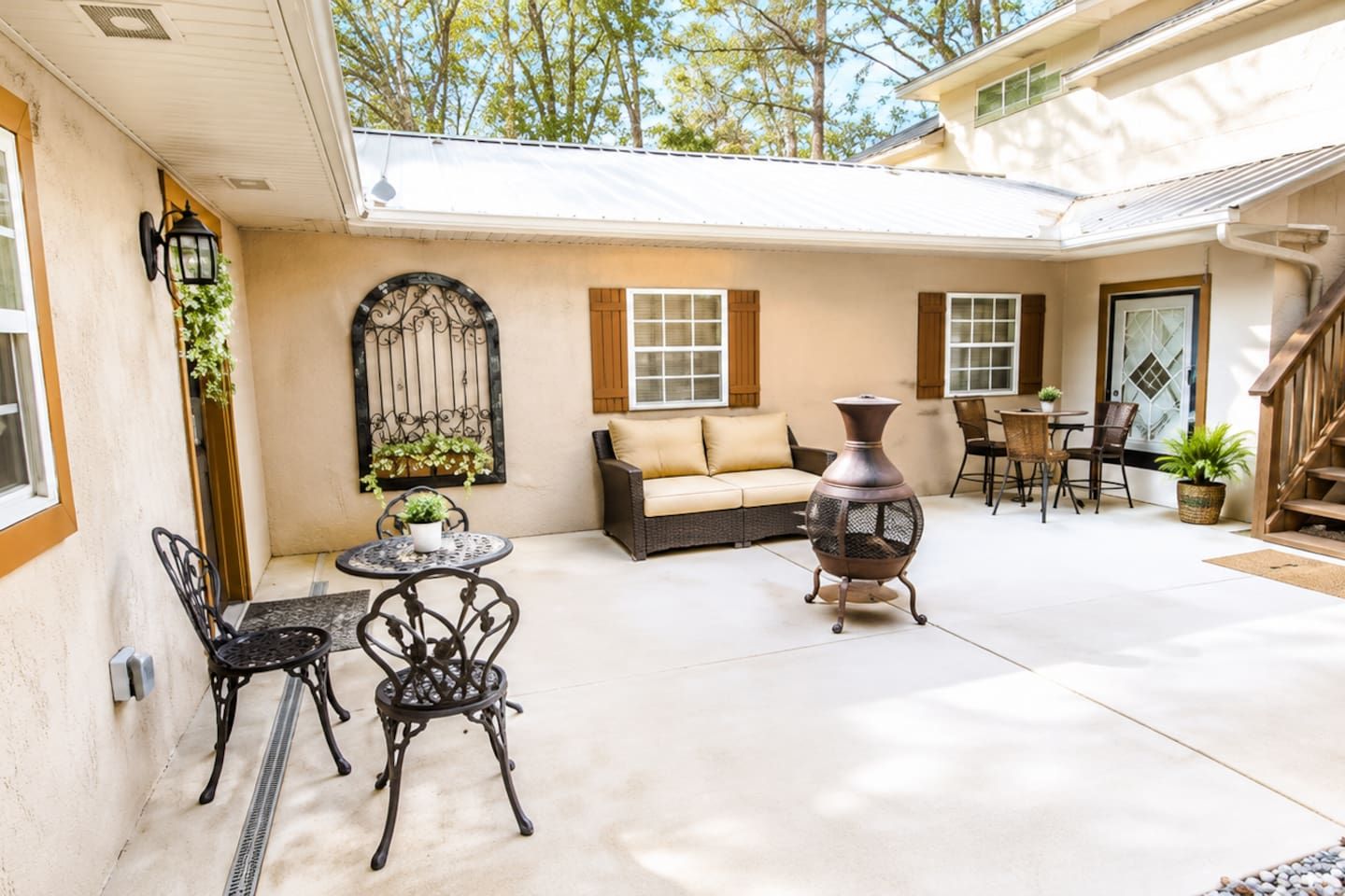 A covered patio area with a sofa, chairs, a table, and a decorative urn.