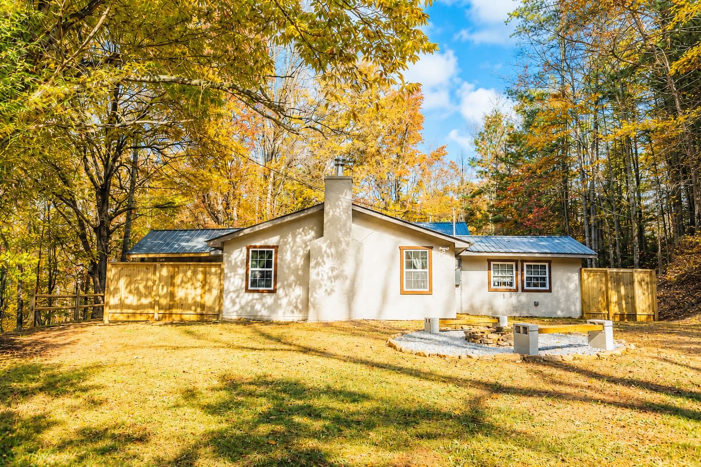 A single-story house with a chimney, a fenced yard, and a clear sky.