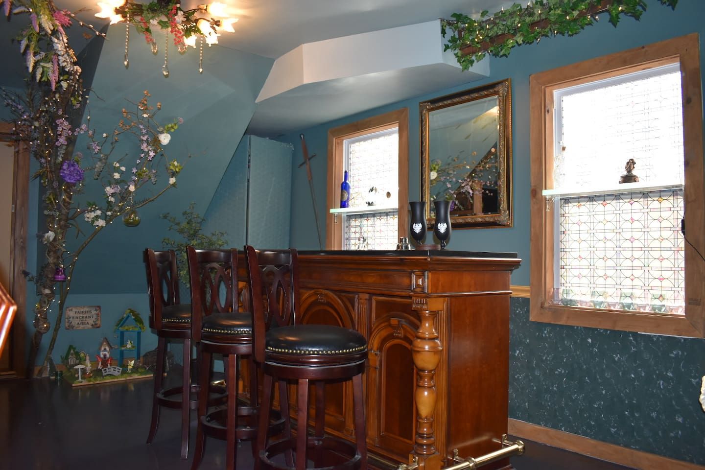 A room with a bar area, wooden chairs, a mirror, and a decorative plant.