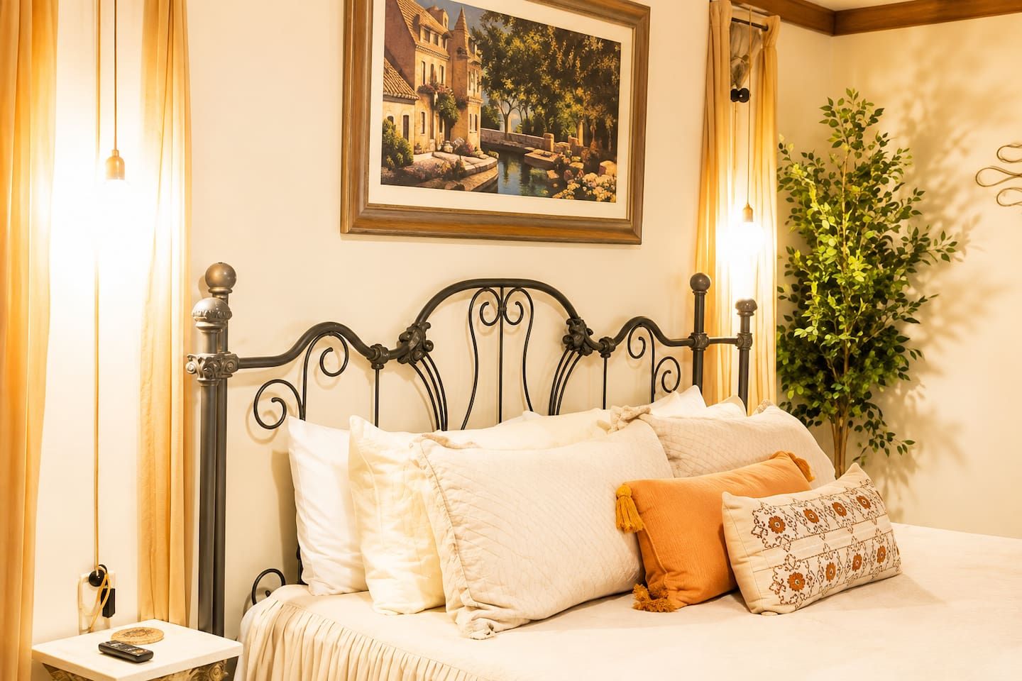 A bed with a black metal headboard, white bedding, and a framed painting above.