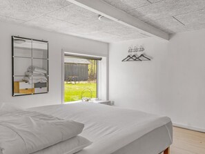 Ein Schlafzimmer mit einem großen Bett, einem Spiegel, einem Fenster und einem Wandhaken für Kleidung.