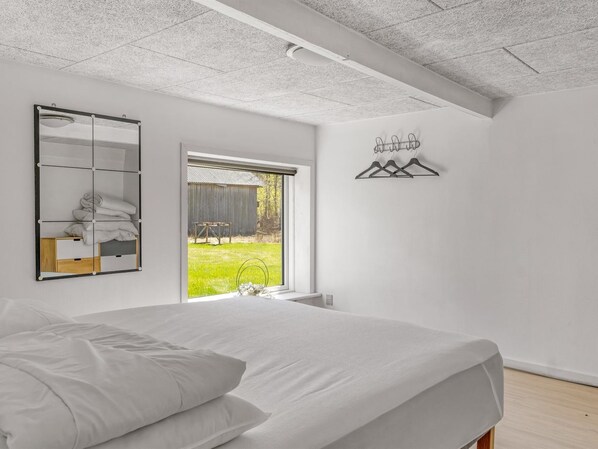 Ein Schlafzimmer mit einem großen Bett, einem Spiegel, einem Fenster und einem Wandhaken für Kleidung.