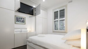 Una camera d'albergo moderna con un letto, una TV a schermo piatto montata a parete, una finestra con persiane e un quadro appeso al muro.