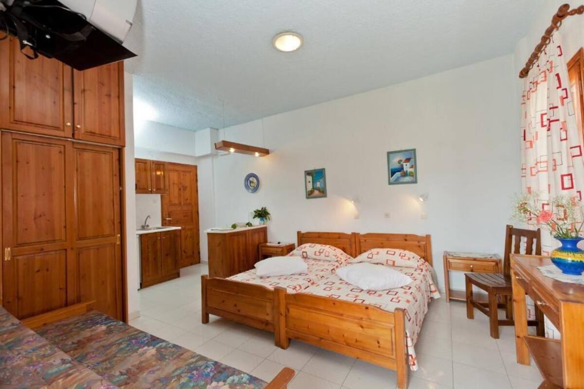A bedroom with a wooden bed, a small desk, a chair, and a wooden wardrobe.