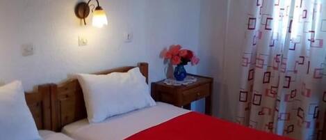 Habitación de hotel con dos camas, una mesita de noche con lámpara, un cuadro en la pared y una cortina estampada.