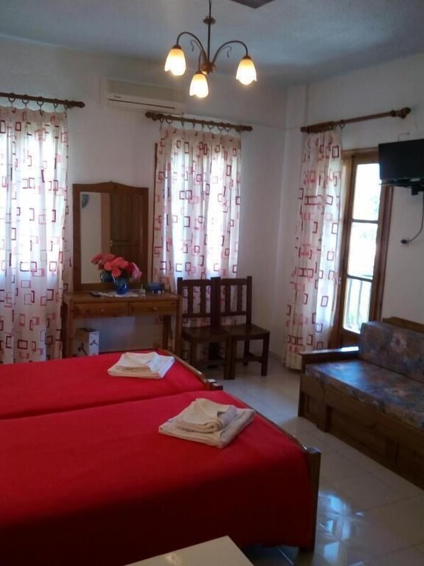 A room with two beds, a desk with a mirror, a chair, a sofa, and a TV mounted on the wall. - Sofia's Garden by Booking Kottas (Skopelos)