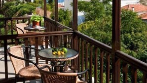 Un balcón techado con mobiliario de mimbre y una mesa, con vistas a un paisaje montañoso.