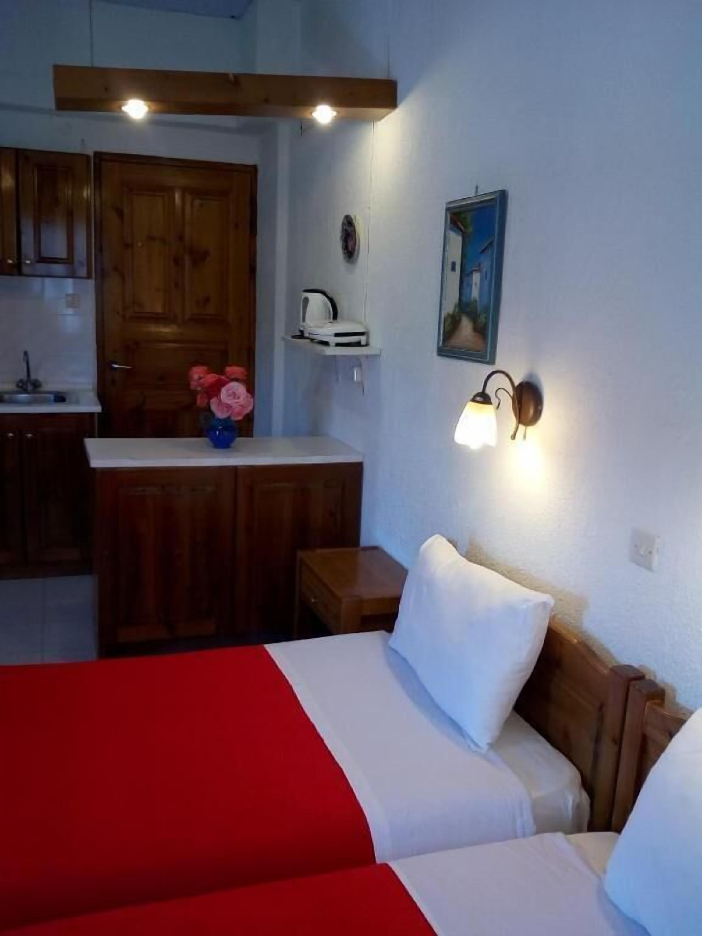 Une chambre comprenant un lit, un petit bureau, une chaise, une étagère avec une bouilloire, un tableau au mur et des armoires en bois.