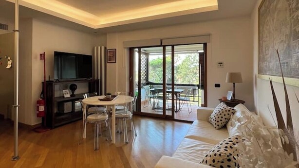 Een moderne woonkamer met een bank, een eettafel met stoelen, een flatscreen televisie en een schuifpui naar een buitenruimte.