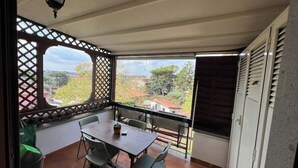 Een balkon met een tafel en stoelen, uitzicht op de omgeving, en een lattenconstructie.