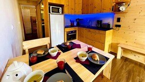 A wooden cabin-style kitchen with a dining table set for breakfast, including bread, butter, and beverages. - Appartment 4 people - Cîmes Scolette (Aussois)
