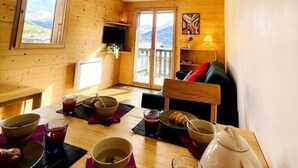 A cozy wooden room with a dining table set for breakfast, a television, and a view of mountains through a window. - Appartment 4 people - Cîmes Scolette (Aussois)