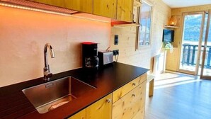A modern kitchen with wooden cabinets, a black countertop, and a large window. - Appartment 4 people - Cîmes Scolette (Aussois)