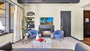 Una sala de estar moderna con chimenea, dos sillones azules, un sofá y un ventanal con persianas.