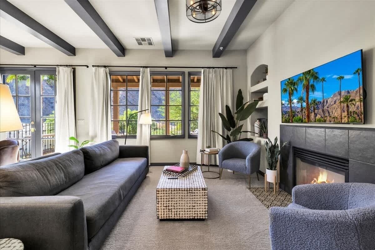 Una sala de estar moderna con chimenea, un ventanal con cortinas, un sofá, una mesa de centro y un televisor montado en la pared.