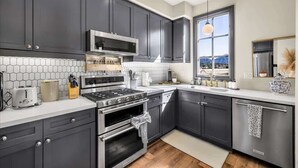 Una cocina moderna con armarios oscuros, una estufa de acero inoxidable y un amplio ventanal con vistas.