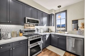 A modern kitchen with dark cabinets, a stainless steel stove, and a large window offering a view. - Legacy Hideaway A | 1BR Legacy Villa (La Quinta)