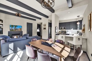 A modern living room with a sofa, dining table, and chairs. There is a kitchen area with cabinets and appliances. - Legacy Hideaway A | 1BR Legacy Villa (La Quinta)