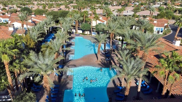 Vista aérea de um resort com uma piscina central rodeada por palmeiras e espreguiçadeiras.
