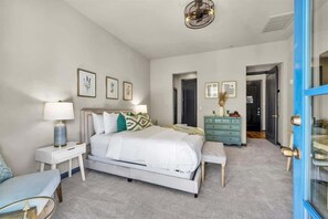 A bedroom with a bed, bedside tables, a dresser, and a door leading to another room. - Legacy Hideaway B | Studio Legacy Villa (La Quinta)