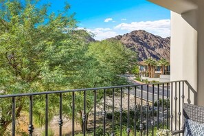 A balcony with a view of a mountain range, a road, and some greenery. - Legacy Hideaway B | Studio Legacy Villa (La Quinta)
