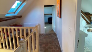 Un pasillo estrecho con techo inclinado, tragaluz y escalera con barandilla de madera.