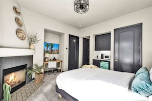 A modern bedroom with a fireplace, a large bed, a desk, and a TV. - Legacy Hideaway C | Studio Legacy Villa (La Quinta)