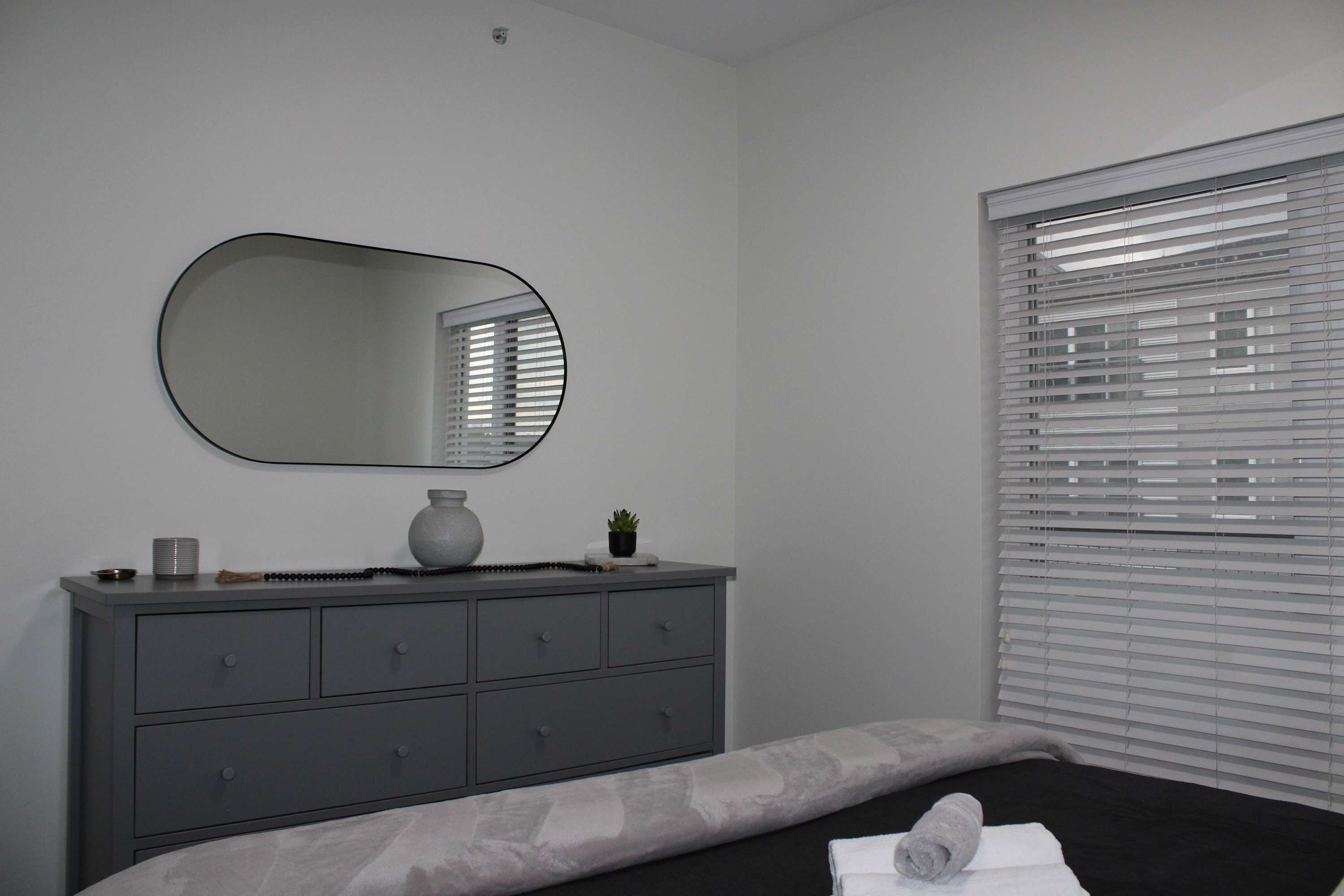 Un dormitorio con cama, cómoda, espejo y ventana con persianas.