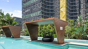 Ein Schwimmbecken mit zwei Holzgebäuden, einem schwarzen Gewebestuhl und einem im Bau befindlichen Gebäude mit Gerüst im Hintergrund.