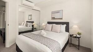 Ein Hotelzimmer mit einem großen Bett, einem Nachttisch mit Lampe, einem kleinen Tisch mit Pflanze und einer Wand-Klimaanlage.
