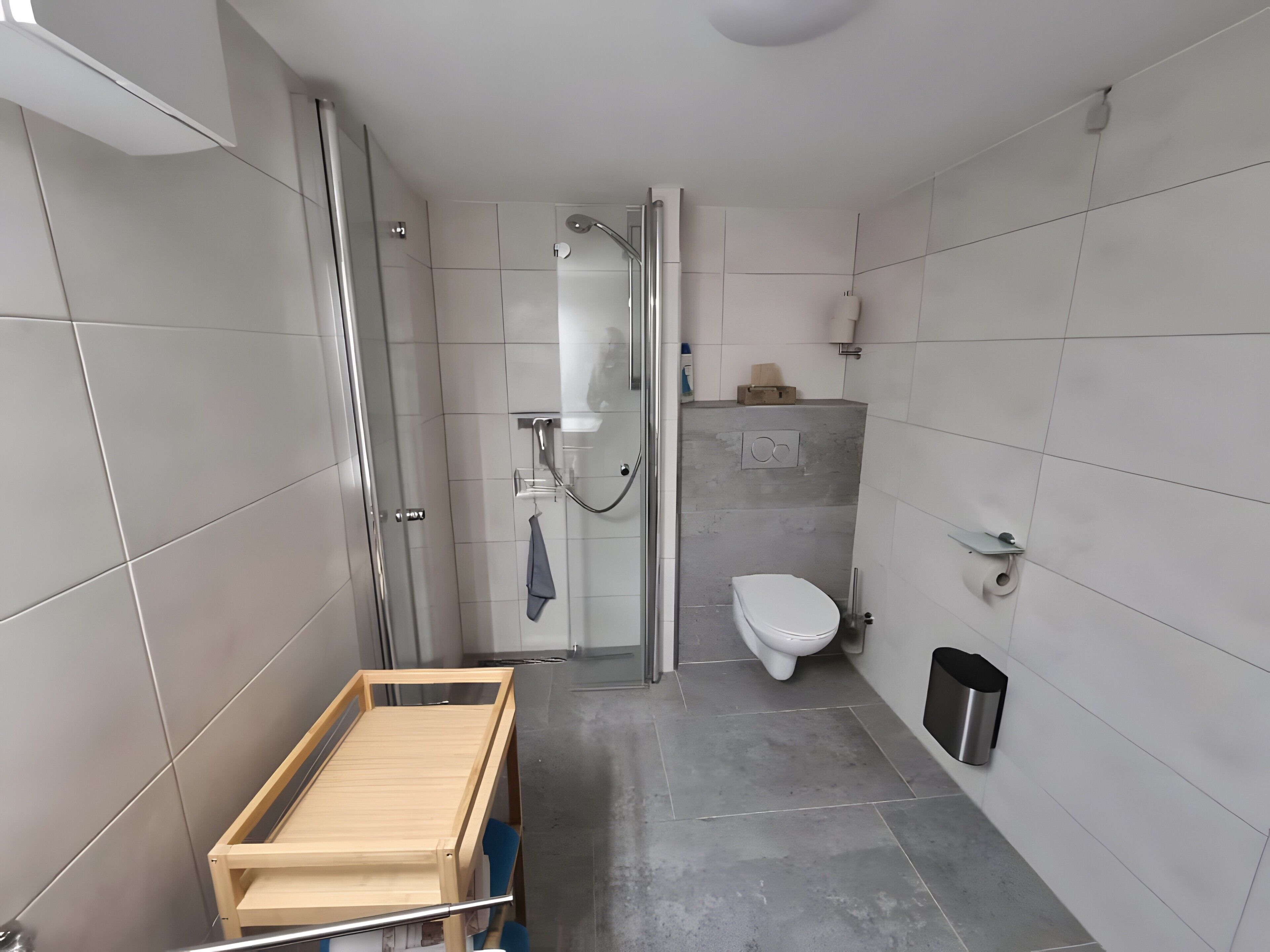 Ein modernes Badezimmer mit Dusche, Toilette und einem Wäscheständer aus Holz.