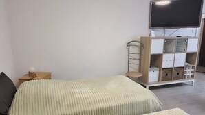 Une chambre avec deux lits, une télévision, une table de chevet et un meuble de rangement.