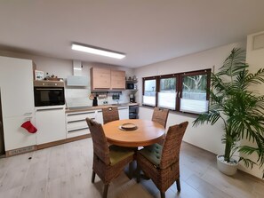 Una cocina moderna con armarios blancos, horno empotrado y comedor con sillas de mimbre y una mesa redonda.