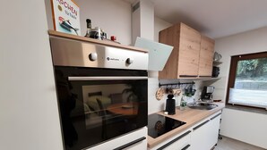 Une cuisine moderne équipée d’un four encastré, d’une machine à café et d’une fenêtre avec des stores.
