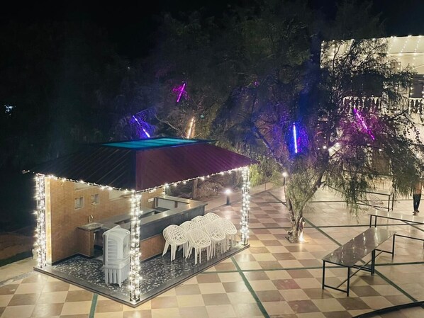 A small outdoor kiosk with a checkered floor, a counter, and white plastic chairs.