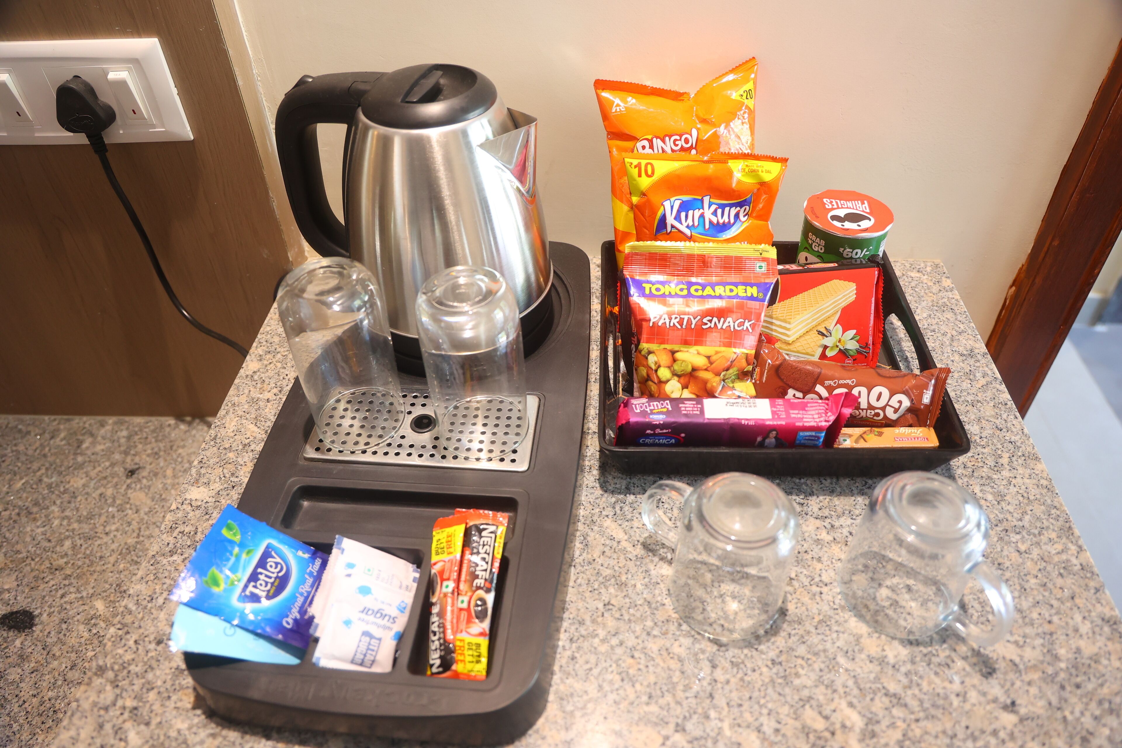 Una encimera de cocina con una tetera, aperitivos y vasos.