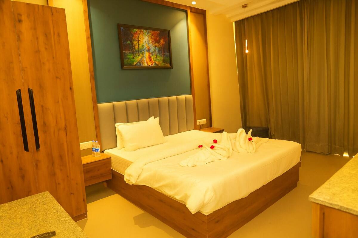 A hotel room with a large bed, a painting on the wall, a wooden wardrobe, and a window with curtains.