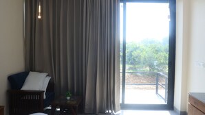 A room with a large sliding glass door leading to an outdoor area, a dark blue chair, a small table with a plant, and a white pillow on the chair. - Skyye Nature Resort (Malakhera)