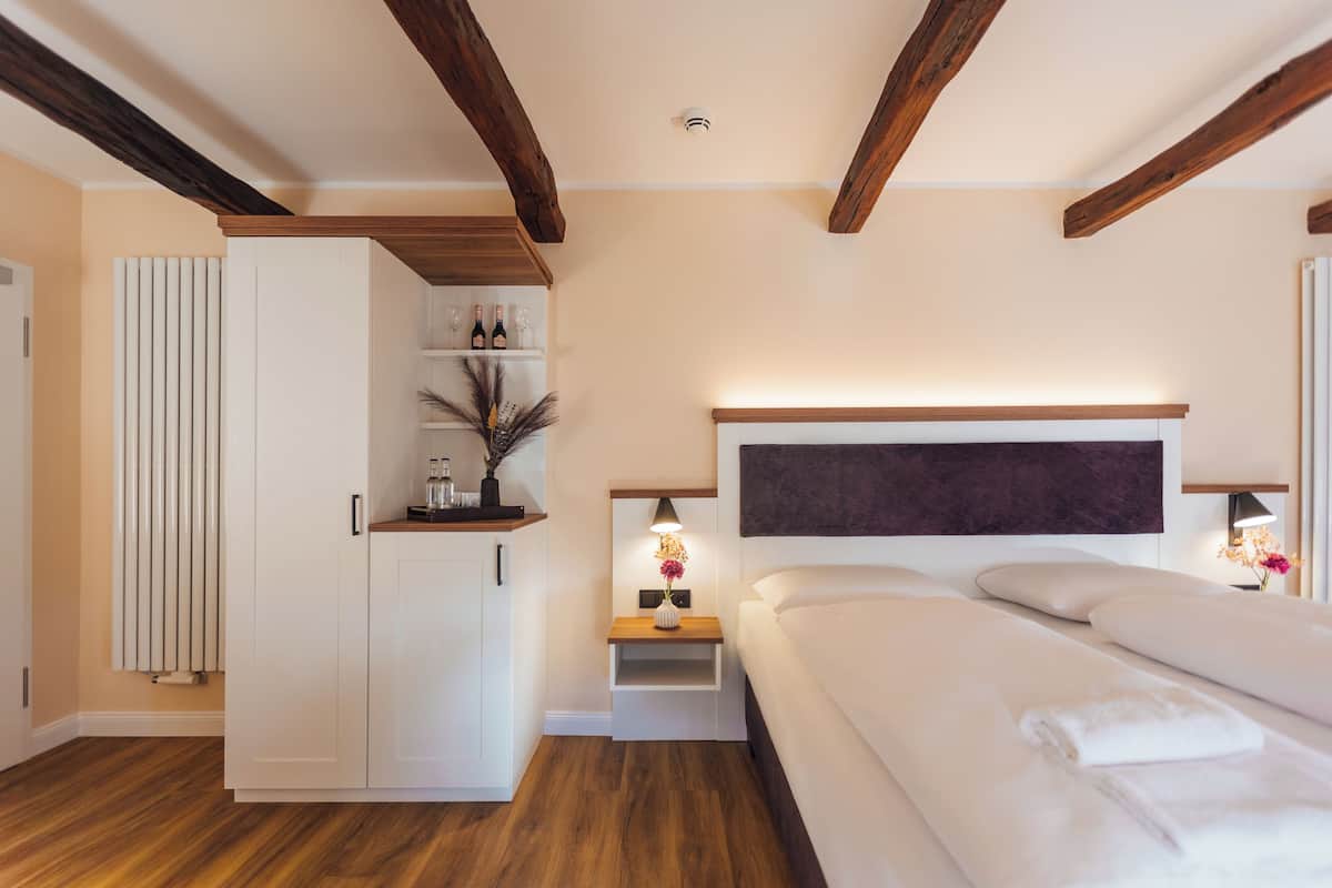 Une chambre avec un plafond en bois, un lit recouvert de draps blancs, une table de chevet avec une lampe et une armoire.