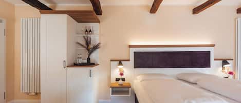 A bedroom with a wooden ceiling, a bed with white linens, a nightstand with a lamp, and a wardrobe.